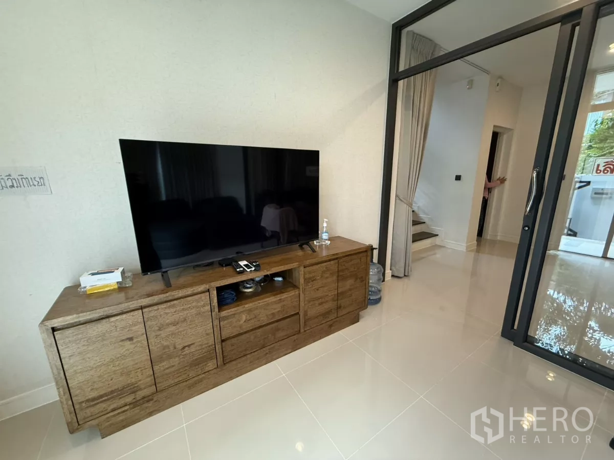 Detached House for rent in Bang Kapi, Bangkok - Living room corner with wooden TV console, glass door, and staircase to the upper floor.