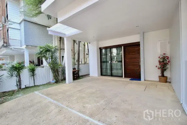 Townhouse for sale in Suan Luang, Bangkok - Covered carport and sliding glass entry beside a small green yard.