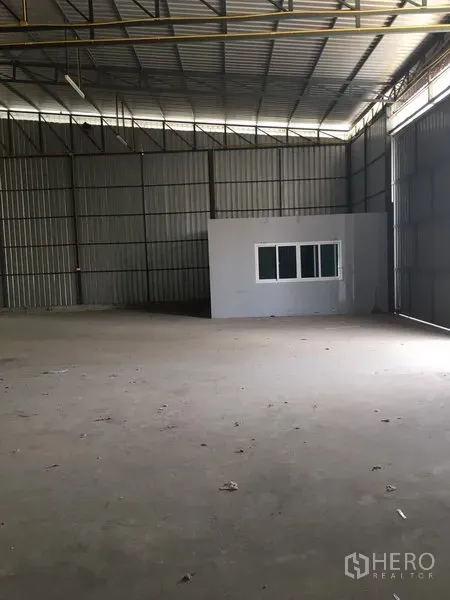 Warehouse for rent in Bang Kapi, Bangkok - Warehouse bay showing a built-in office with window, tall corrugated metal walls, and wide sliding access door.