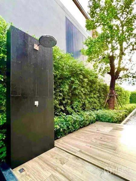 Detached House for sale in Huai Khwang, Bangkok - Outdoor rain shower on a sleek black panel beside a timber deck and lush green hedges.