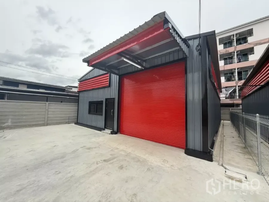 Warehouse for rent in Lat Phrao, Bangkok - Modern warehouse exterior in Lat Phrao with red roller shutter doors and a wide concrete loading yard.