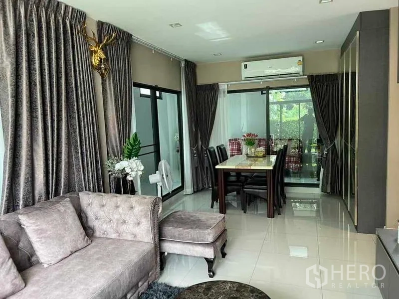 Detached House for sale in Khan Na Yao, Bangkok - Open-plan living and dining room with plush sofa, dining table, large curtains and air conditioner.
