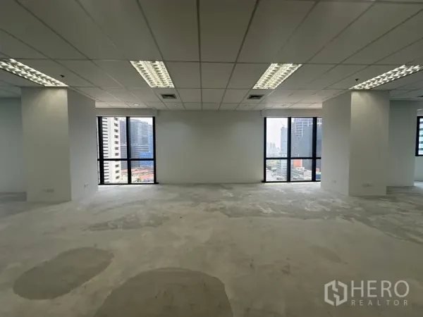 Office Space for rent in Bang Rak, Bangkok - Bright office floor with large windows, city views and fluorescent lighting over a concrete subfloor.