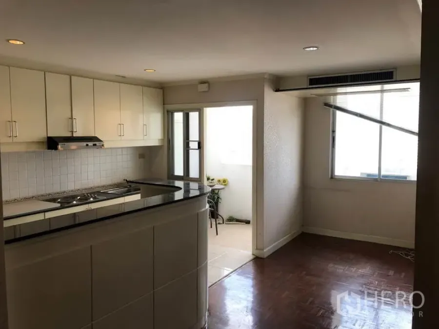 Condominium for sale in Watthana, Bangkok - Open-plan living area with white kitchen cabinets, breakfast bar, and door to a small balcony.