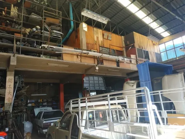 Warehouse for rent in Yan Nawa, Bangkok - High-ceiling warehouse interior with mezzanine storage racks, steel truss roof and parked pickup trucks.