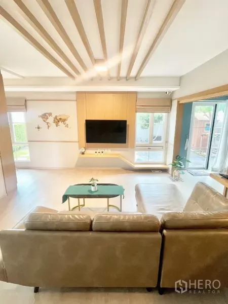 Detached House for rent in Prawet, Bangkok - Bright living room with L-shaped sofa, wall-mounted TV and wood slat ceiling.