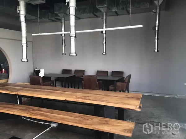 Retail Space for rent in Watthana, Bangkok - Open dining area with wooden communal tables, hanging ventilation ducts and grey walls.