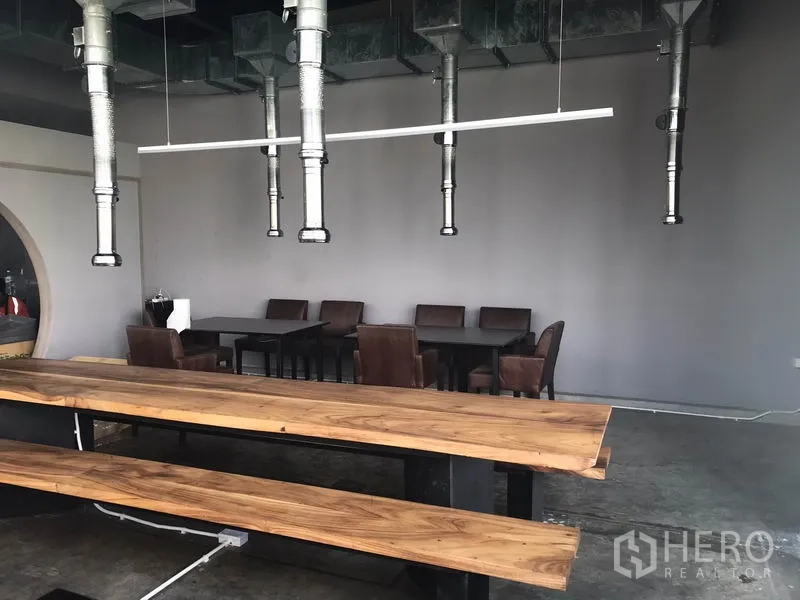 Retail Space for rent in Watthana, Bangkok - Open dining area with wooden communal tables, hanging ventilation ducts and grey walls.