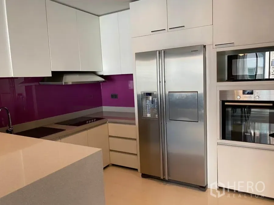 Condominium for rent in Khlong Toei, Bangkok - Modern L-shaped kitchen with white cabinets, vivid magenta backsplash, induction cooktop and stainless side-by-side fridge.