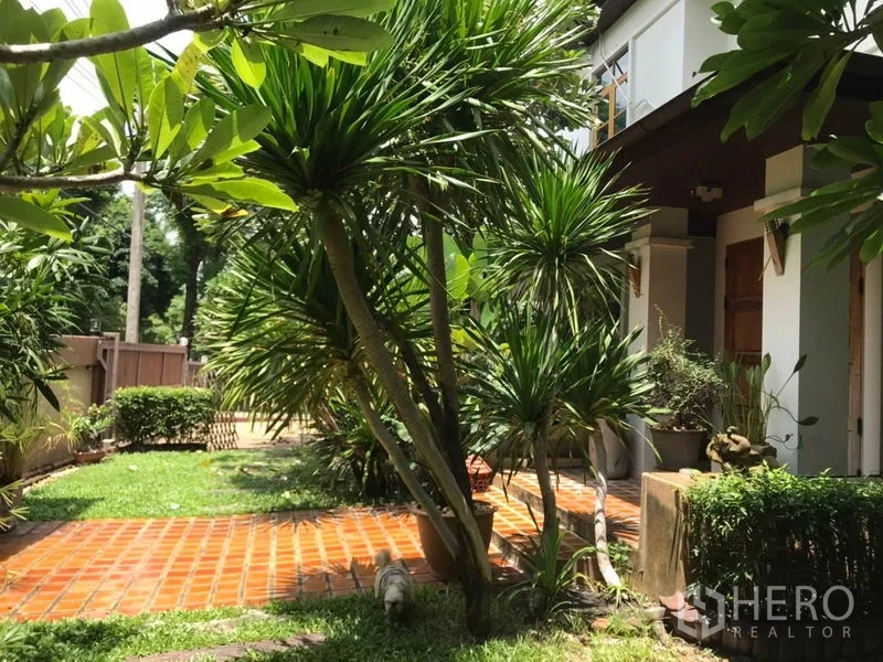 Detached House for sale in Lat Phrao, Bangkok - Front garden with tiled walkway, tropical plants and covered porch of the house.