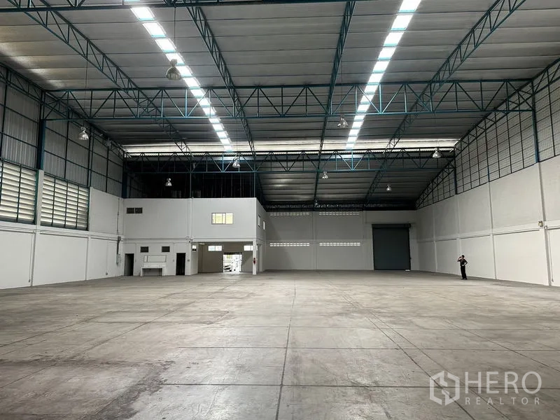 Factory for rent in Si Racha, Chon Buri - Warehouse interior facing the loading roller door with office block to the side and wide concrete floor.