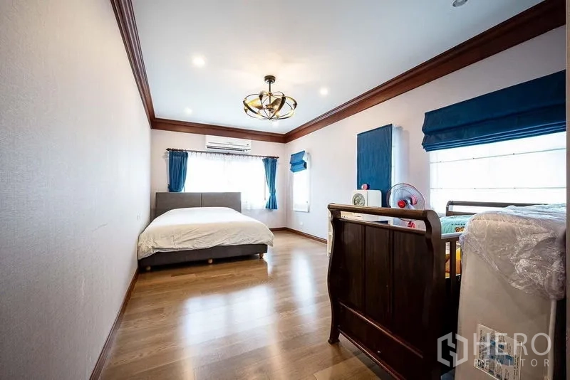Detached House for sale in Prawet, Bangkok - Large family bedroom with crib, blue curtains and wood flooring.