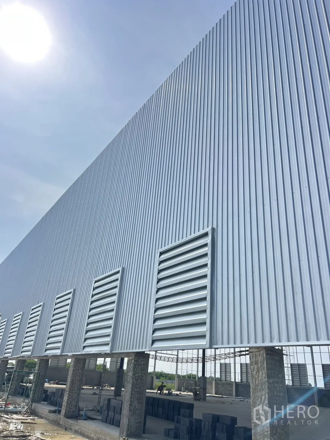 Factory for rent in Mueang Samut Prakan, Samut Prakan - Long exterior wall with multiple louvered vents above raised columns at a construction site.