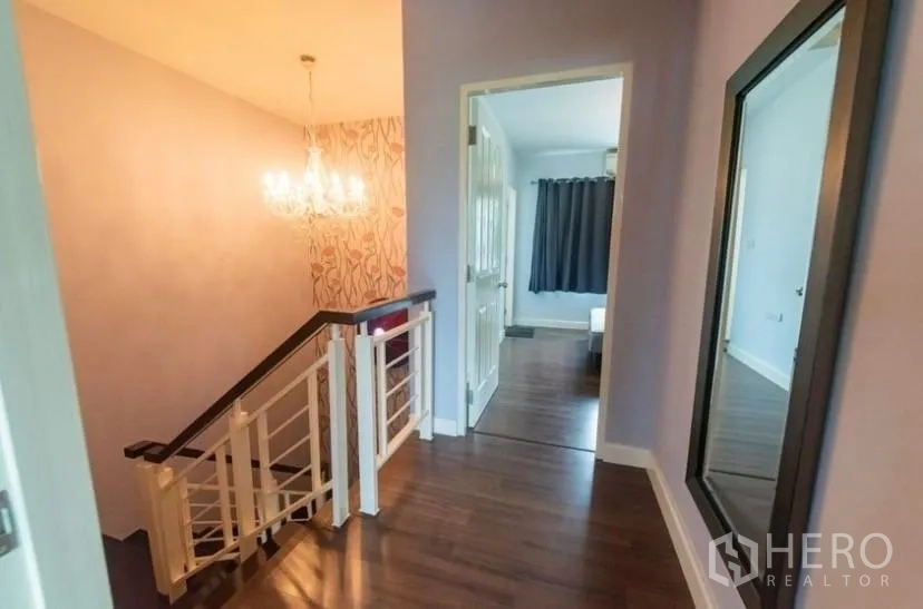 Townhouse for rent in Suan Luang, Bangkok - Upper hallway with chandelier above the staircase and a full-height mirror.