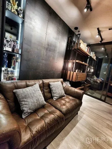 Condominium for sale in Pathum Wan, Bangkok - Living area with leather sofa, track lighting, and industrial-style feature wall.
