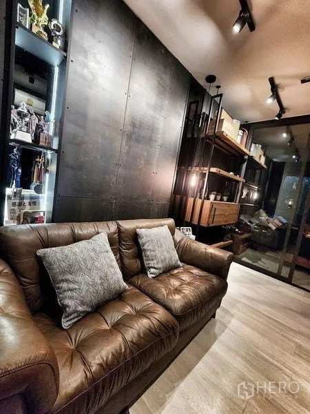 Condominium for sale in Pathum Wan, Bangkok - Living area with leather sofa, track lighting, and industrial-style feature wall.
