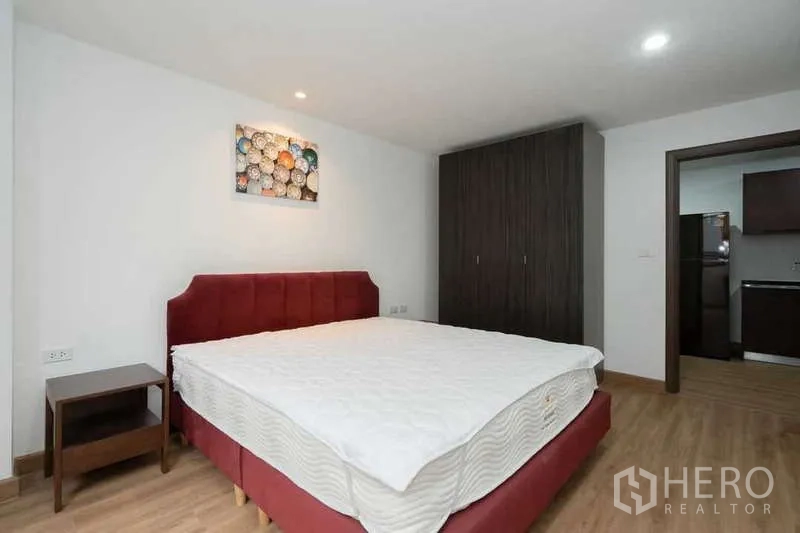 Apartment for rent in Khlong Toei, Bangkok - Master bedroom angle showing wardrobe, bedside table and entry toward the kitchen.