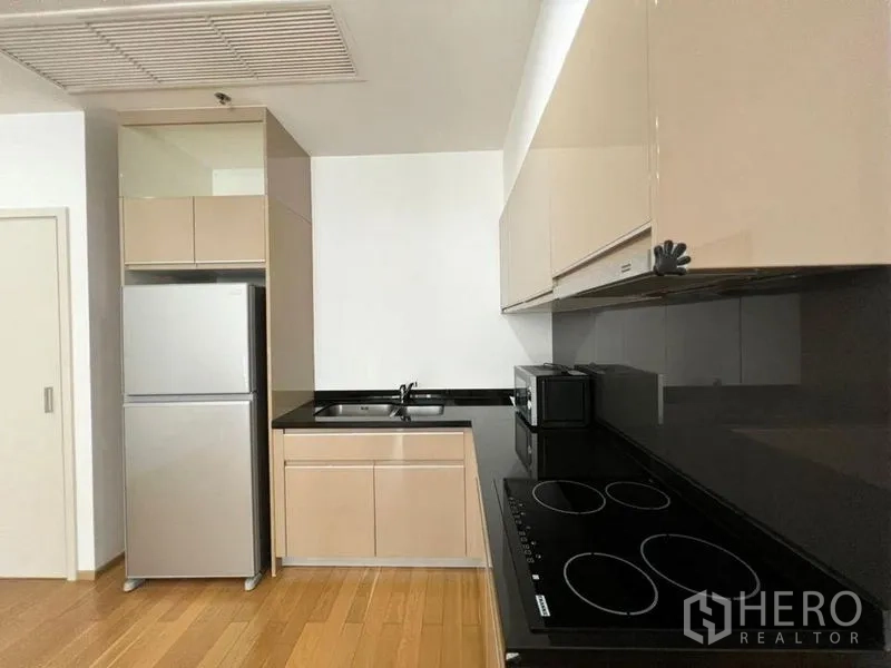 Condominium for rent in Khlong Toei, Bangkok - Modern kitchen with glossy cabinets, black stone countertop, electric hob, microwave and full-size fridge.
