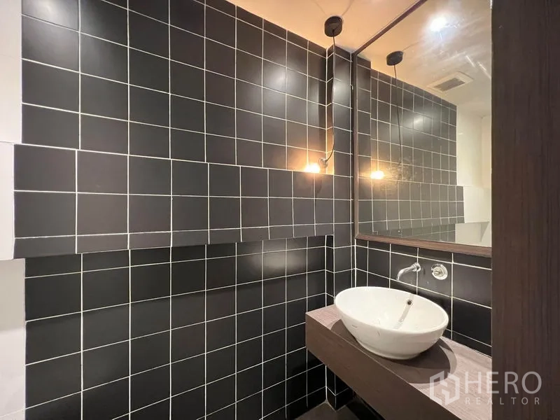 Shophouse for rent - Modern restroom with black tiled walls and a vessel sink.