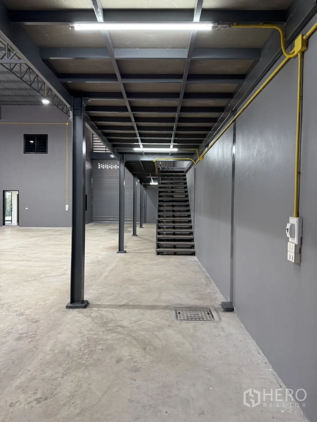 Warehouse for rent in Lam Luk Ka, Pathum Thani - Under-mezzanine aisle with steel columns and exposed conduits.