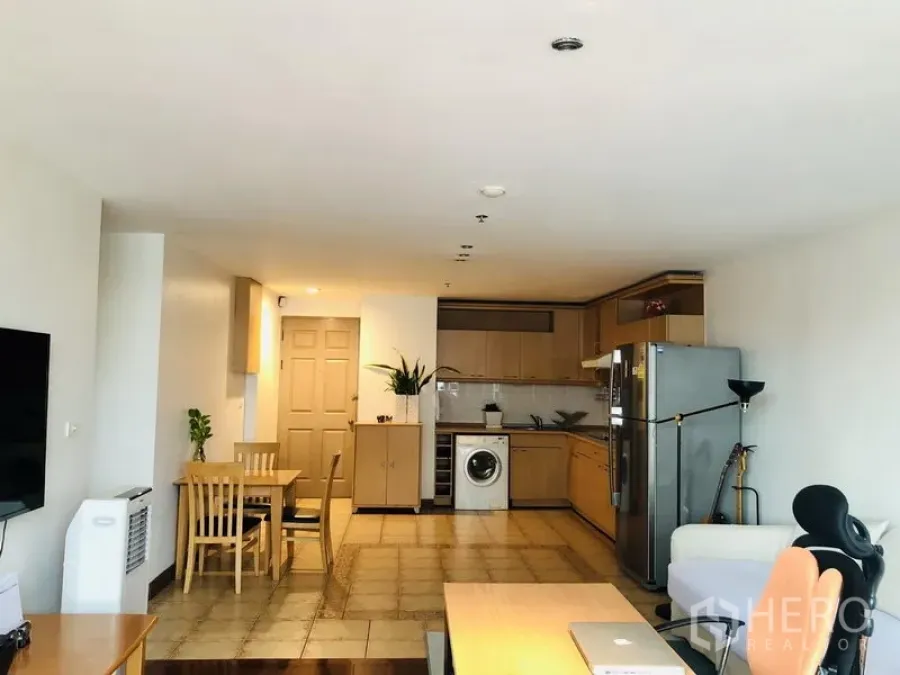 Condominium for rent in Pathum Wan, Bangkok - Open-plan living area with dining set and L-shaped kitchen with washer and fridge.