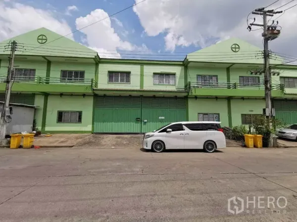 โรงงาน ให้เช่าในSamut Sakhon - ด้านหน้าโรงงาน ประตูเหล็กบานใหญ่สีเขียว มีรถตู้สีขาวจอดริมถนน