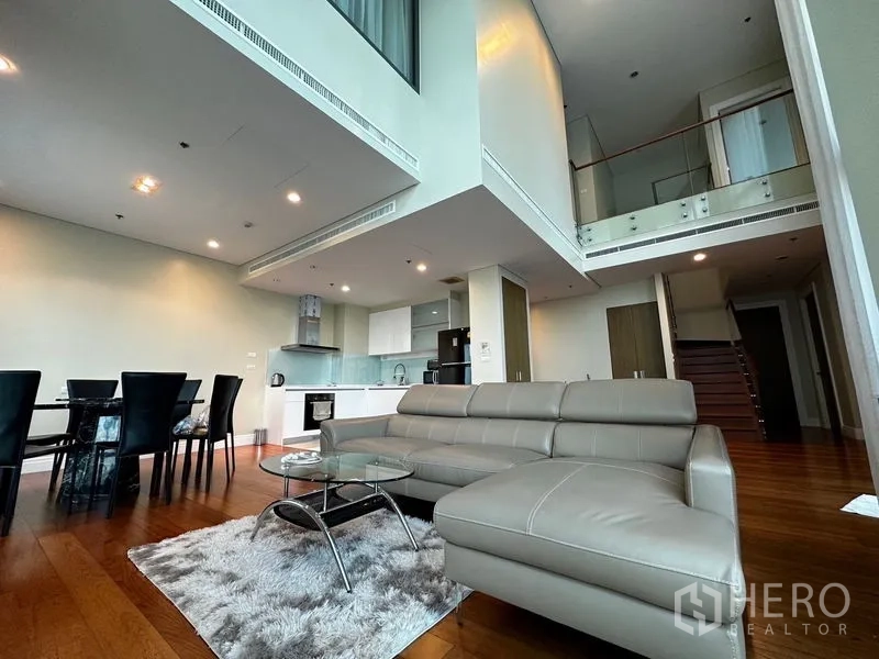 Condominium for rent in Khlong Toei, Bangkok - Loft-like living area with double-height ceiling, kitchen, dining set and leather sofa.
