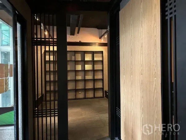 Retail Space for rent in Bang Rak, Bangkok - Entrance corridor leading to a display room with wall-to-wall grid shelving and spotlight tracks.