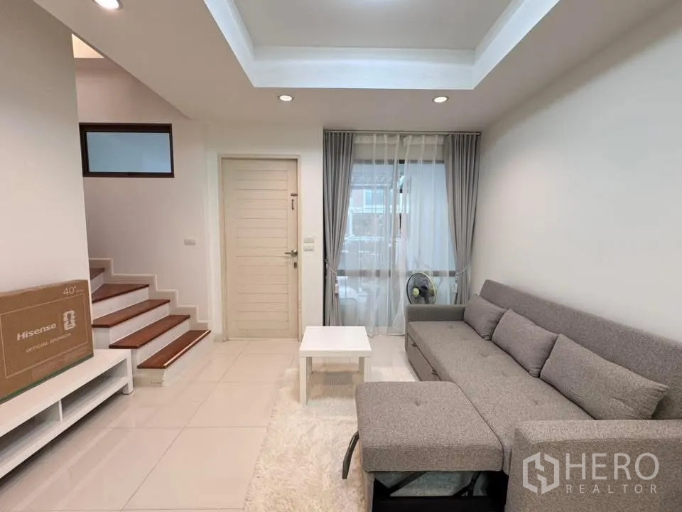Townhouse for rent in Phra Khanong, Bangkok - Living room with sectional sofa, staircase, and large window.