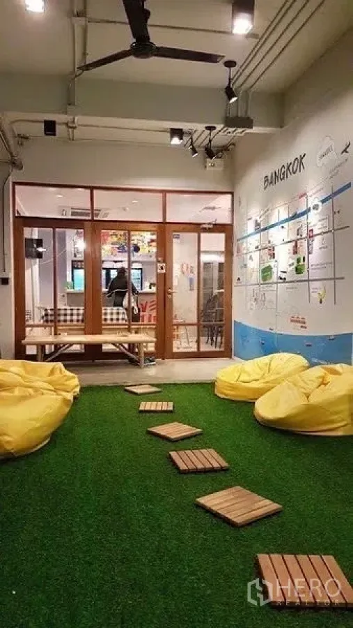 Shophouse for rent in Pathum Wan, Bangkok - Indoor garden lounge with artificial grass, yellow beanbags, wooden stepping pads and a glass meeting room with a Bangkok map mural.