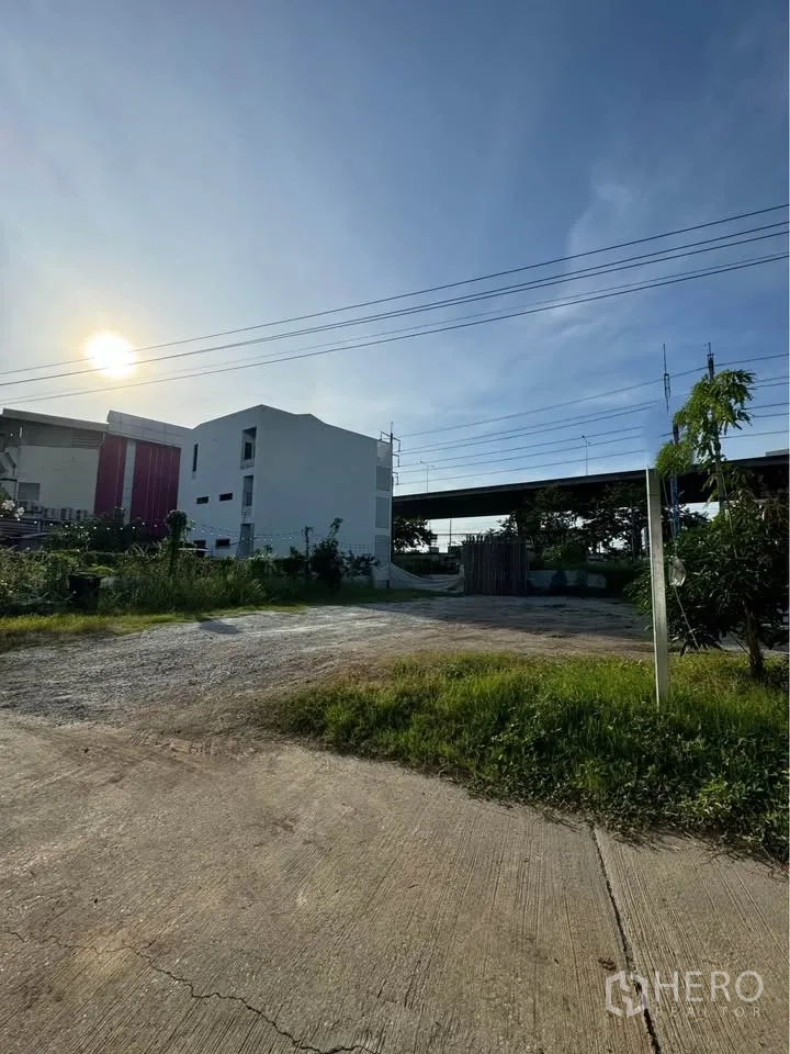 土地 for rent in Bang Na, Bangkok - 混凝土车道通向平整土地，四周有植被并设有入口大门。
