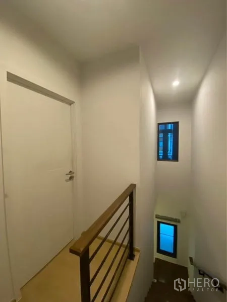 Townhouse for rent in Prawet, Bangkok - Stair landing with metal handrail, white walls and a narrow vertical window.