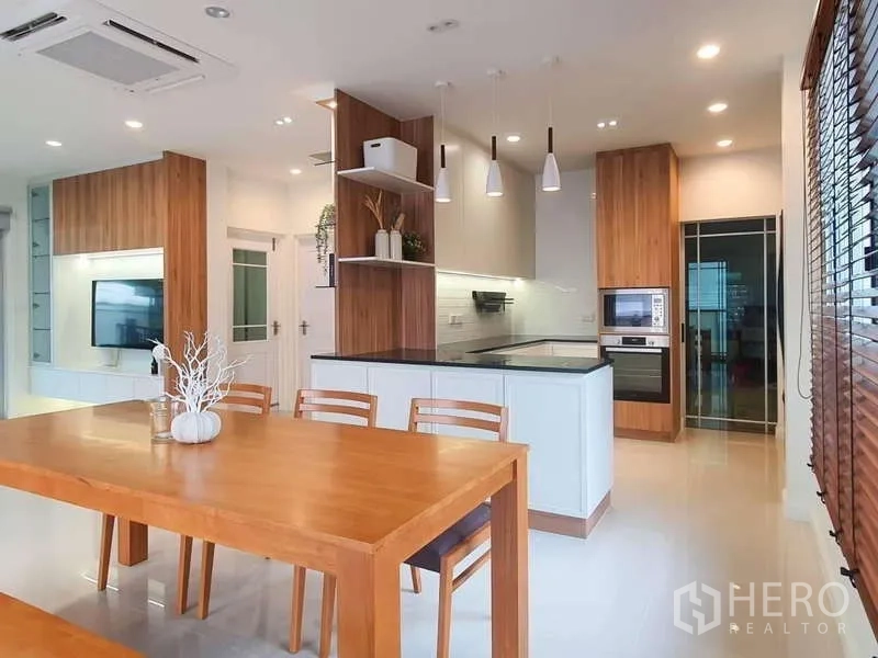 Detached House for rent in Sathon, Bangkok - Kitchen with peninsula counter, pendant lighting, and adjacent wooden dining set.
