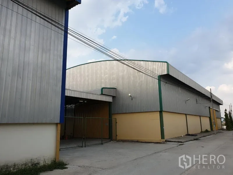 Warehouse for rent in Lat Krabang, Bangkok - Corner exterior of sheet-metal warehouse with gated loading area and canopy entrance.