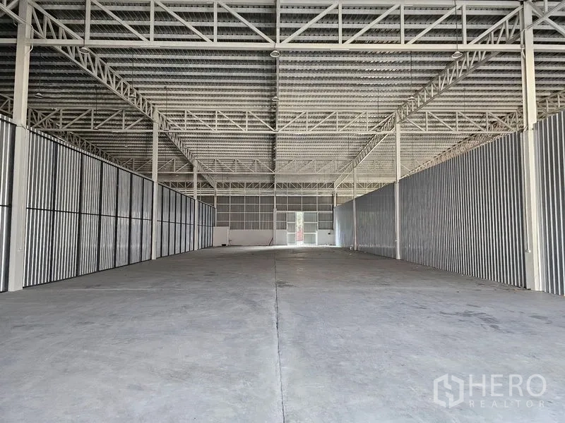 Warehouse for rent in Khlong Toei, Bangkok - Deep warehouse interior showing steel beams, concrete floor and daylight from the rear door.