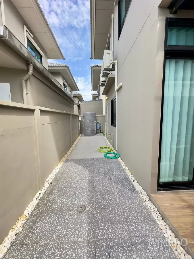 Detached House for rent in Samut Prakan - Side utility walkway with tiled floor, water tank and garden hose.