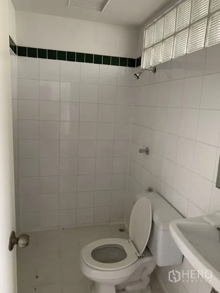 Shophouse for rent in Bang Na, Bangkok - Clean tiled bathroom with toilet, sink, and glass-block window for light.