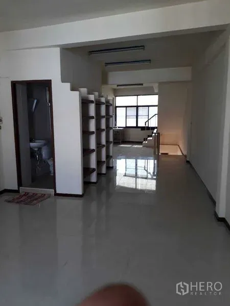 Shophouse for rent in Suan Luang, Bangkok - Open-plan shophouse floor with glossy tiles, built-in shelving, window light and a small bathroom.