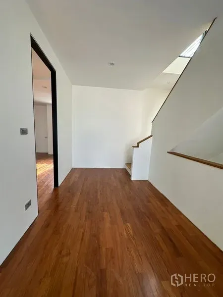 Detached House for rent in Watthana, Bangkok - Upper-floor landing with wooden flooring, clean white walls, and a staircase illuminated by natural light.