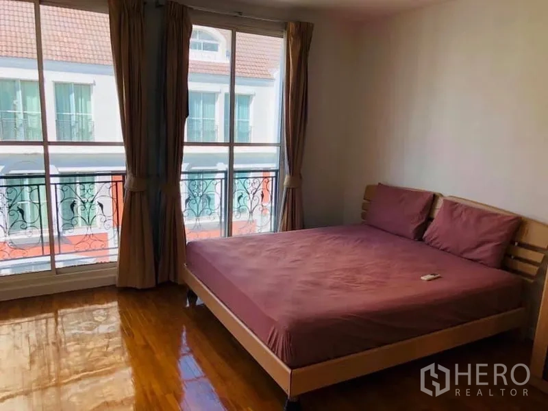 Townhouse for rent in Khlong Toei, Bangkok - Bedroom with queen bed and floor-to-ceiling windows opening to a Juliet balcony.