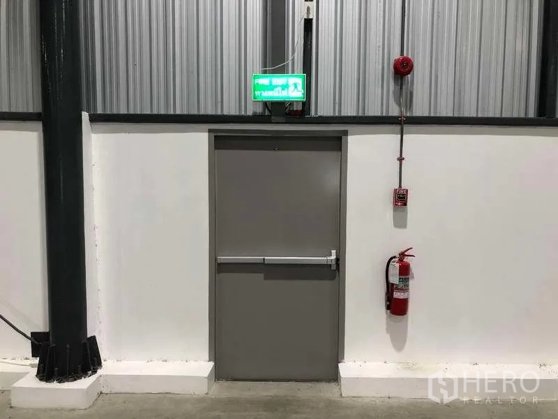 Factory for rent in Bang Sao Thong, Samut Prakan - Emergency exit door with fire extinguisher and alarm inside the factory.