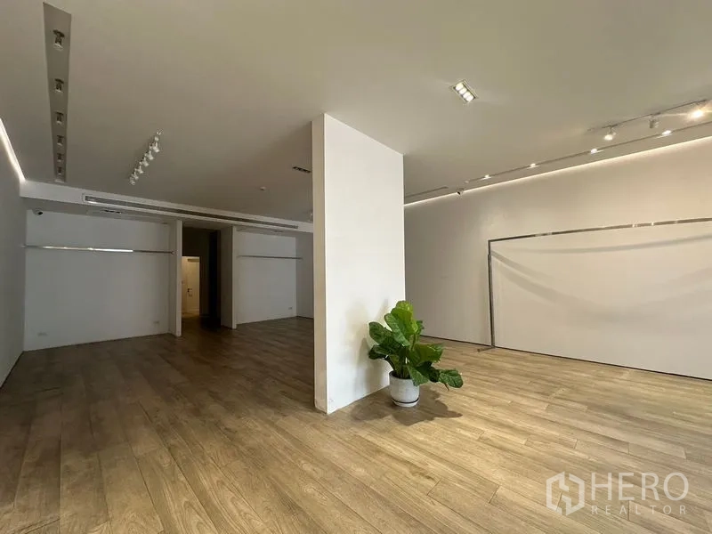 Home Office for rent in Phra Khanong, Bangkok - Spacious hall with center column, plant and warm wood floors under spotlights.