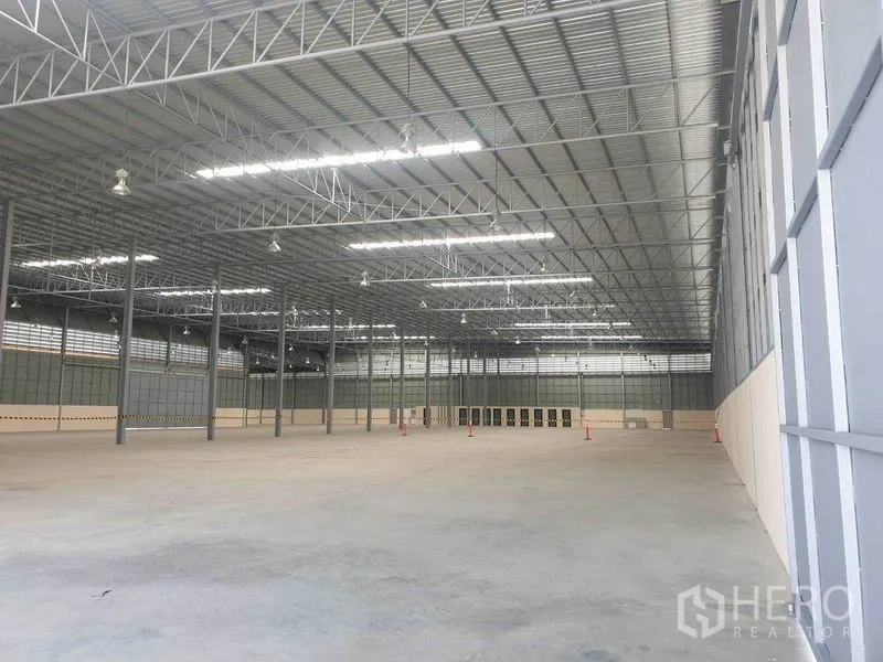 Warehouse for rent in Chachoengsao - Expansive warehouse interior with high steel truss roof, skylights and smooth concrete floor.