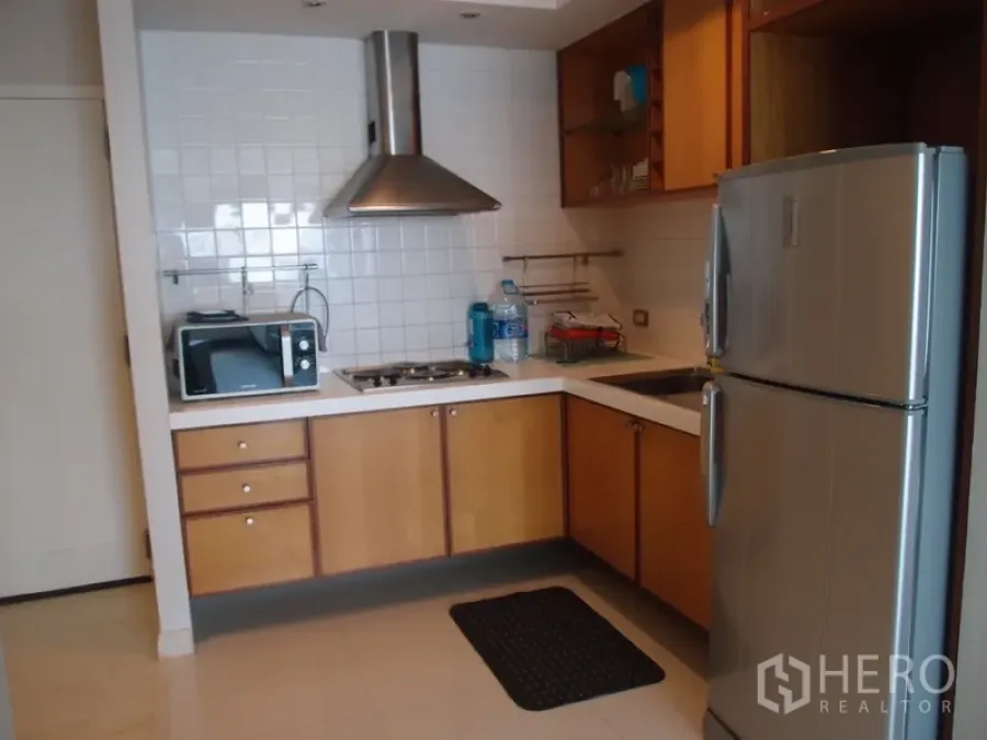 Condominium for rent in Sathon, Bangkok - Modern L-shaped kitchen with stainless refrigerator, gas hob, range hood, microwave, and white tile backsplash in a Sathon condominium.
