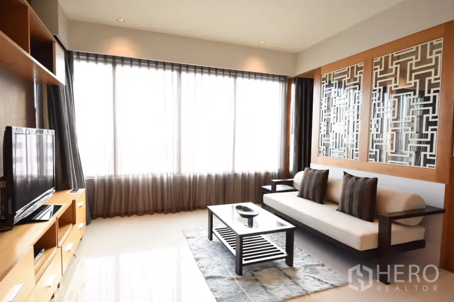 Condominium for rent in Khlong Toei, Bangkok - Bright living room with wall-to-wall windows, sheer curtains, modern sofa and a glass coffee table.