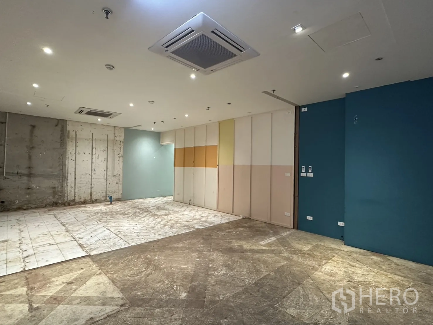 Retail Space for rent in Watthana, Bangkok - Wide view of the open-plan unit showing ceiling AC, spotlights, a color-panel wall and concrete surfaces.