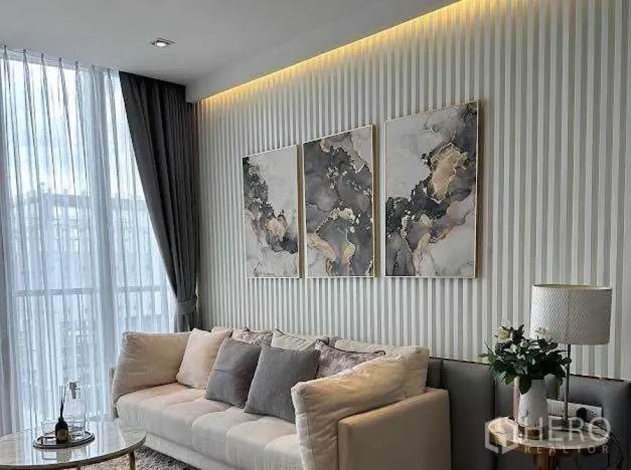 Condominium for sale in Khlong Toei, Bangkok - Lounge with light-toned sofa, textured feature wall, and triptych artwork.