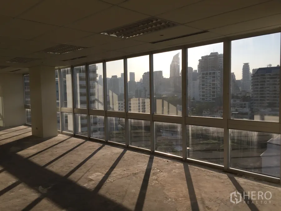 Office Space for rent in Khlong Toei, Bangkok - Corner shell office with floor-to-ceiling windows and Bangkok skyline views, afternoon light across concrete floor.