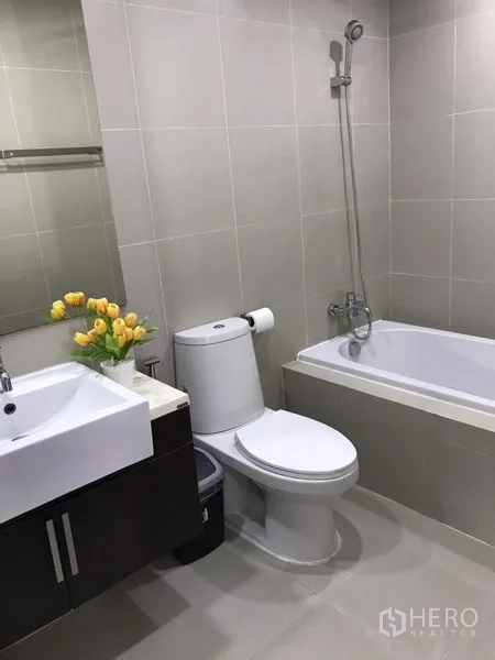 Condominium for rent in Khlong Toei, Bangkok - Contemporary bathroom with bathtub, shower, vanity and neutral tiles.