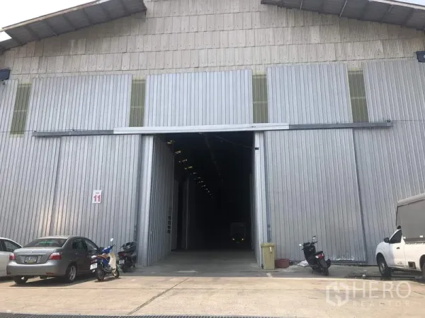 Warehouse for rent in Pak Kret, Nonthaburi - Large sliding-door entrance of a metal-clad warehouse with parking area at the front in Pak Kret, Nonthaburi.